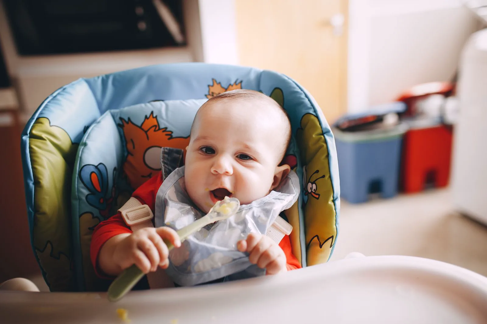 Baby im Hochstuhl beim Essen mit einem Löffel